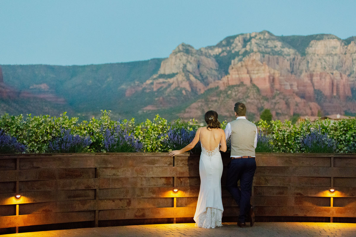 A bride and groom gaze upon rocky formations near Sedona from a patio lined with flowers