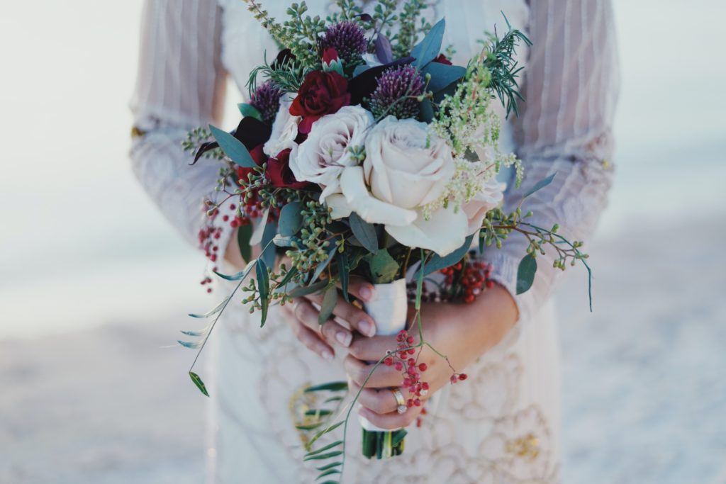 A torso shot of a bride, which focuses on the bouquet of light-colored roses and assorted greenery