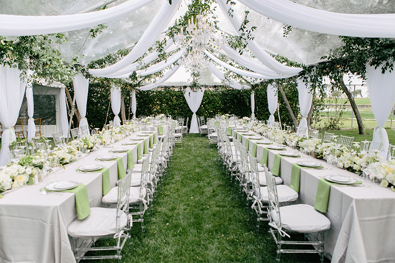 Expensive outdoor garden wedding venue in Arizona with a white tent, draped white fabric, a chandelier and white table and chairs