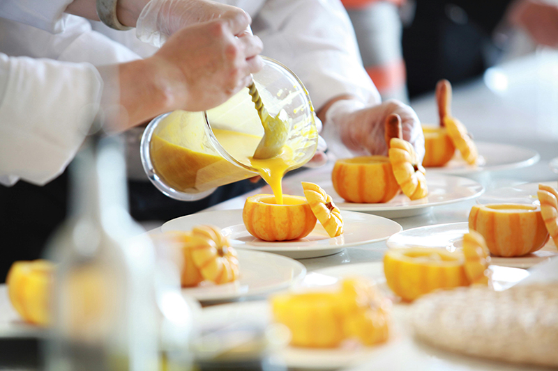 Chef’s pouring pumpkin soup into hollowed out pumpkin shells to show how to elevate a seasonal catering presentation. 
